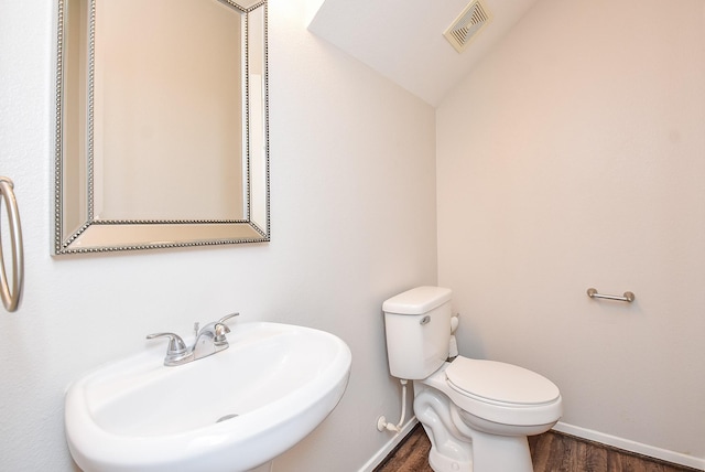 bathroom featuring visible vents, toilet, vaulted ceiling, wood finished floors, and a sink