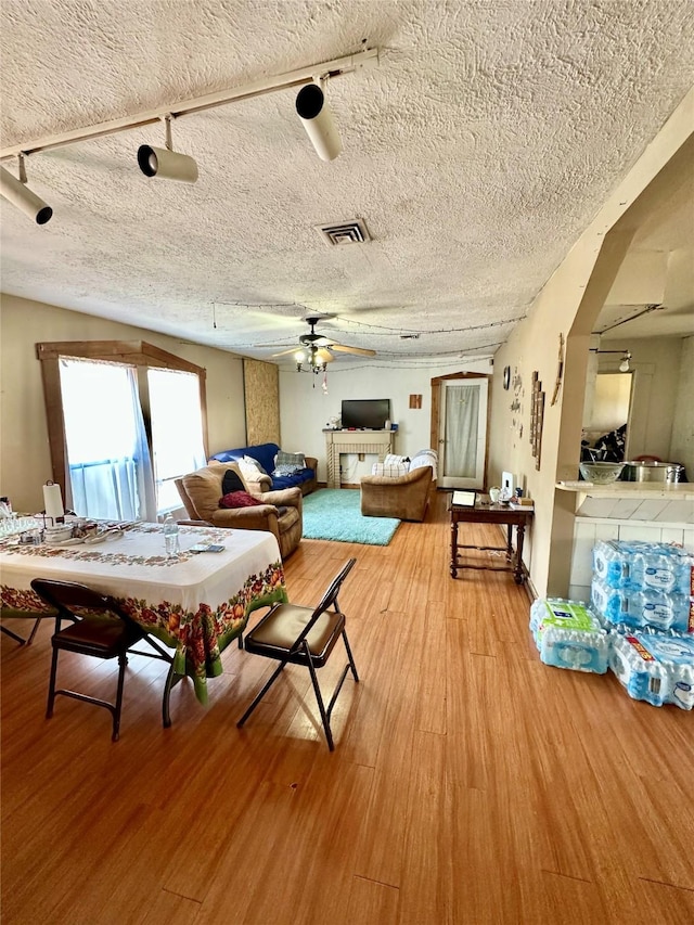 living room featuring light wood finished floors, visible vents, a textured ceiling, and ceiling fan