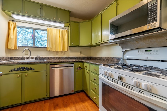 kitchen featuring a sink, stainless steel appliances, dark countertops, and dark wood finished floors