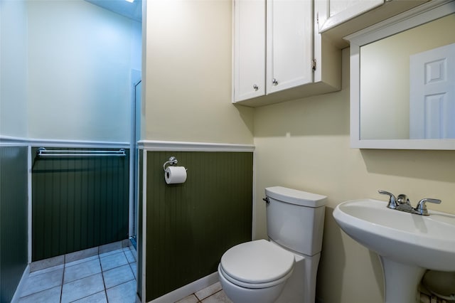 half bath with tile patterned flooring, toilet, a wainscoted wall, and a sink