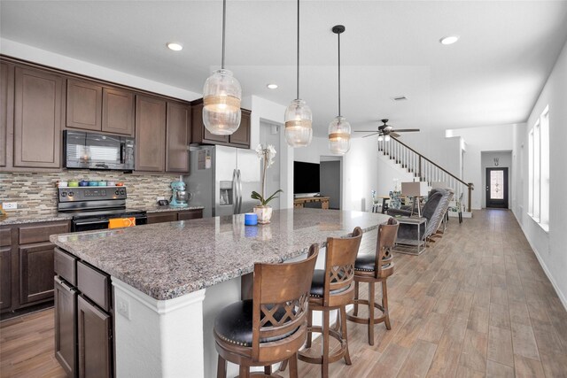 kitchen with black appliances, light wood-type flooring, backsplash, and a kitchen island