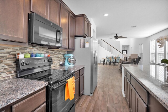 kitchen featuring decorative backsplash, light wood-style flooring, stone countertops, and black appliances