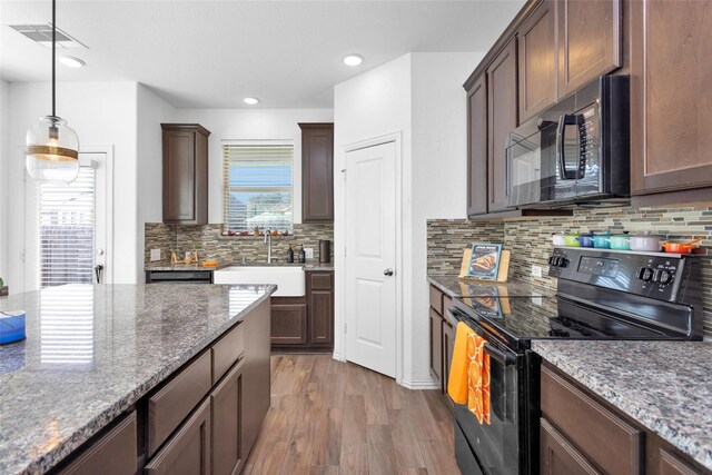 kitchen with visible vents, dark wood finished floors, dark stone counters, a sink, and black appliances