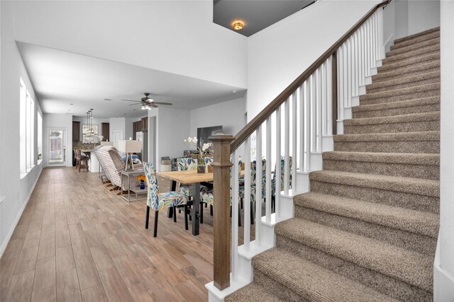 stairs featuring ceiling fan with notable chandelier, wood finished floors, and baseboards