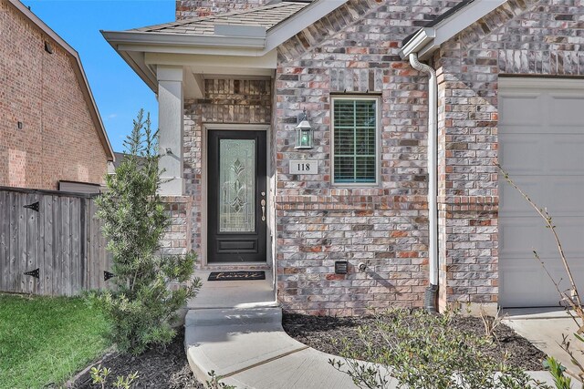 doorway to property with stone siding, an attached garage, and fence