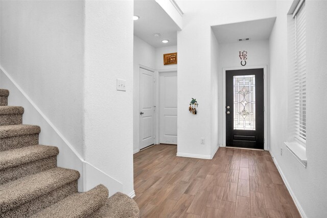 foyer with stairway, visible vents, baseboards, and wood finished floors