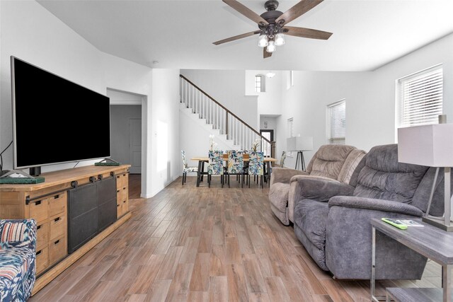 living area with stairs, light wood-style floors, and ceiling fan