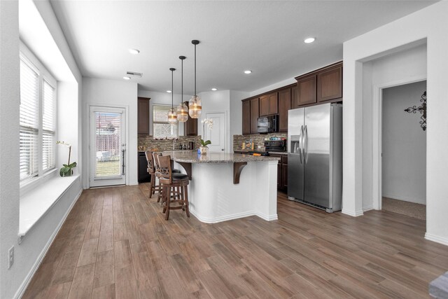 kitchen with wood finished floors, black appliances, dark brown cabinets, a kitchen breakfast bar, and a center island