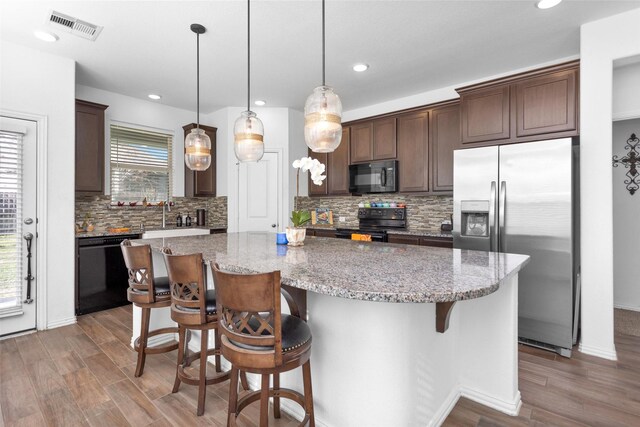 kitchen featuring visible vents, dark brown cabinets, a center island, wood finished floors, and black appliances