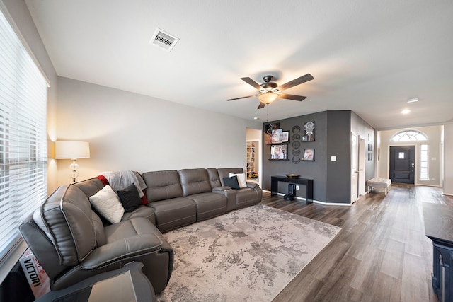 living room with dark wood-style floors, visible vents, baseboards, and ceiling fan