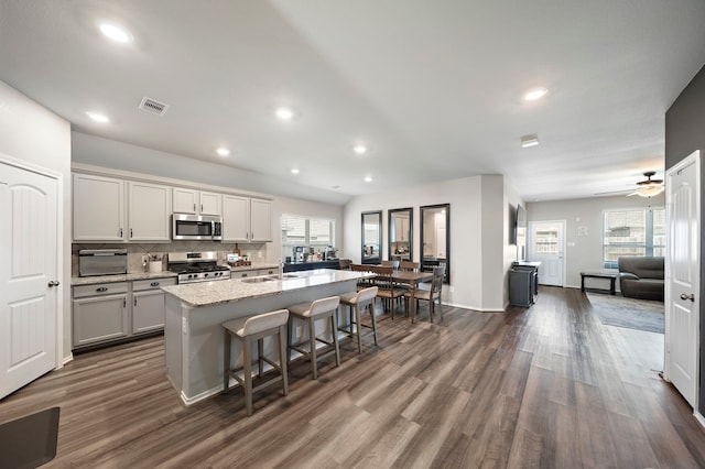 kitchen with visible vents, open floor plan, a breakfast bar, stainless steel appliances, and a kitchen island with sink