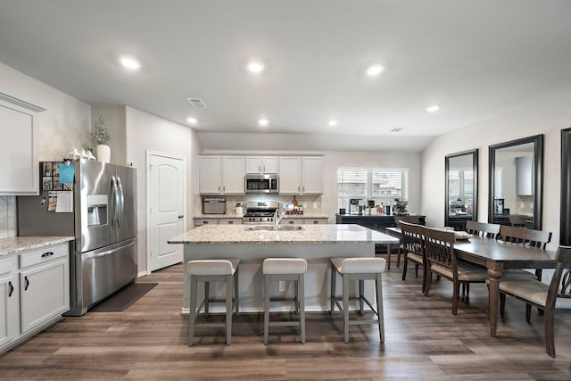 kitchen featuring decorative backsplash, dark wood finished floors, a center island with sink, and stainless steel appliances