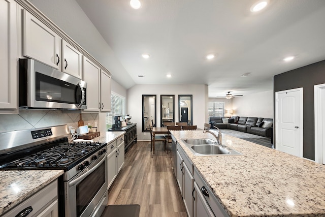 kitchen with wood finished floors, a center island with sink, a sink, appliances with stainless steel finishes, and tasteful backsplash