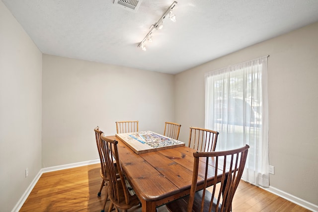 dining space featuring visible vents, baseboards, track lighting, light wood-style floors, and a textured ceiling