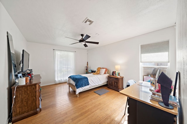 bedroom with visible vents, a textured ceiling, ceiling fan, and light wood finished floors