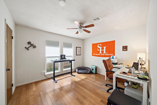 home office with visible vents, a textured ceiling, light wood-type flooring, and ceiling fan