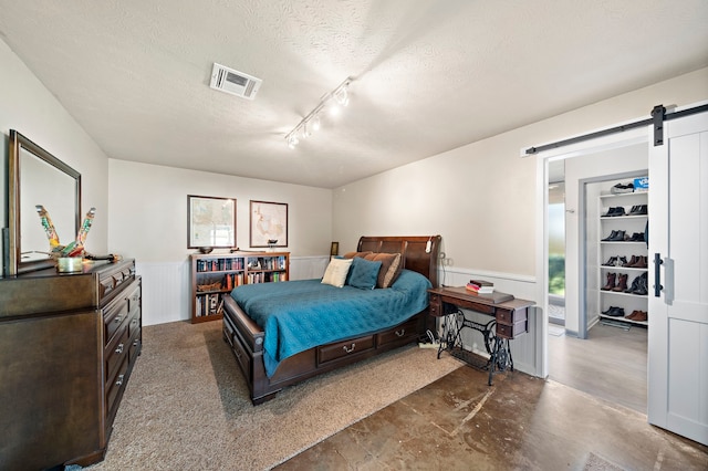 bedroom featuring visible vents, a wainscoted wall, concrete flooring, a barn door, and a textured ceiling