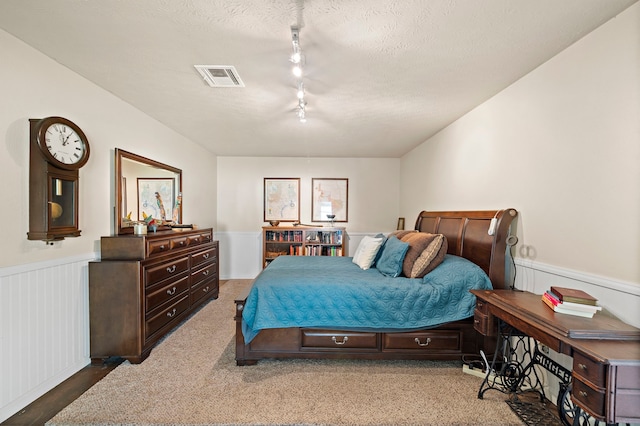 bedroom featuring visible vents, a textured ceiling, track lighting, and wainscoting