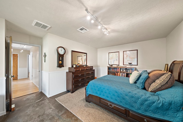 bedroom with visible vents, a textured ceiling, concrete floors, and wainscoting