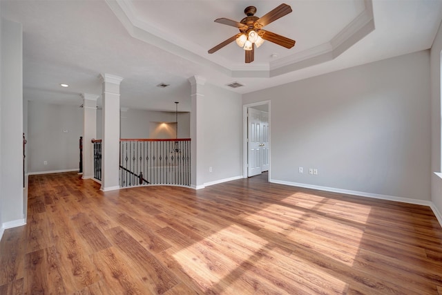 empty room featuring ornamental molding, a tray ceiling, wood finished floors, baseboards, and ceiling fan