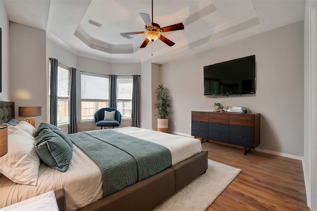 bedroom with visible vents, ornamental molding, wood finished floors, baseboards, and a raised ceiling