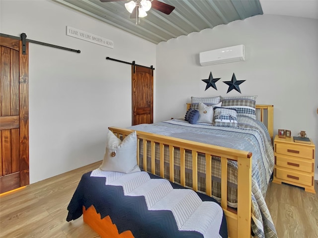 bedroom with ceiling fan, an AC wall unit, a barn door, and wood finished floors