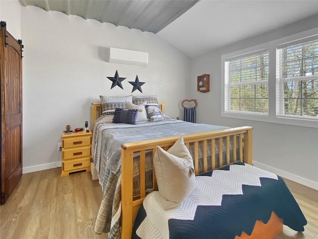 bedroom with a wall mounted air conditioner, a barn door, light wood-style floors, baseboards, and vaulted ceiling