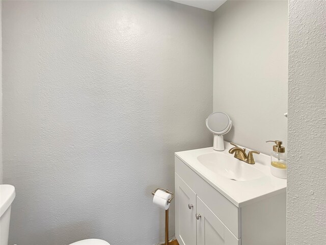 bathroom with vanity, toilet, and a textured wall