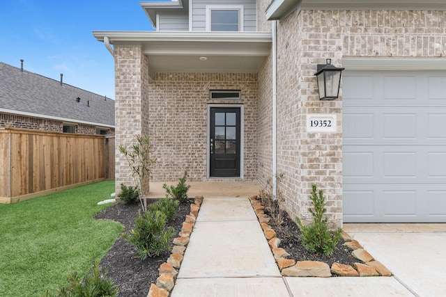 view of exterior entry featuring an attached garage, fence, brick siding, and a yard