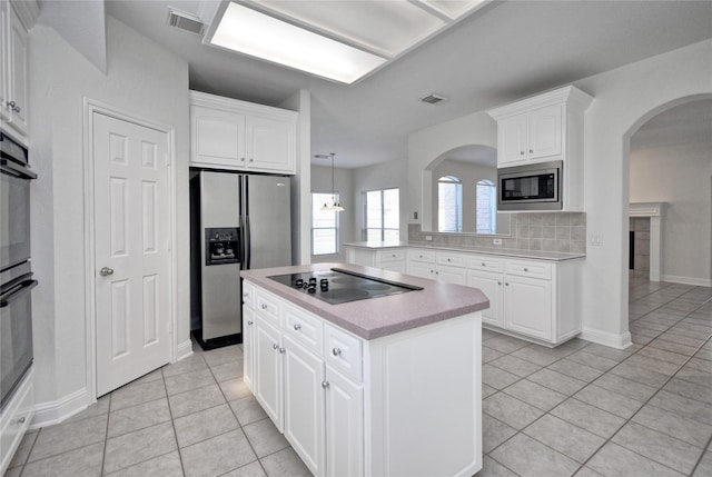 kitchen with light tile patterned floors, a kitchen island, arched walkways, light countertops, and appliances with stainless steel finishes