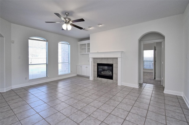 unfurnished living room featuring light tile patterned floors, a ceiling fan, baseboards, and a tile fireplace