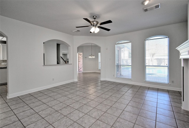 unfurnished living room with visible vents, baseboards, light tile patterned flooring, and ceiling fan with notable chandelier