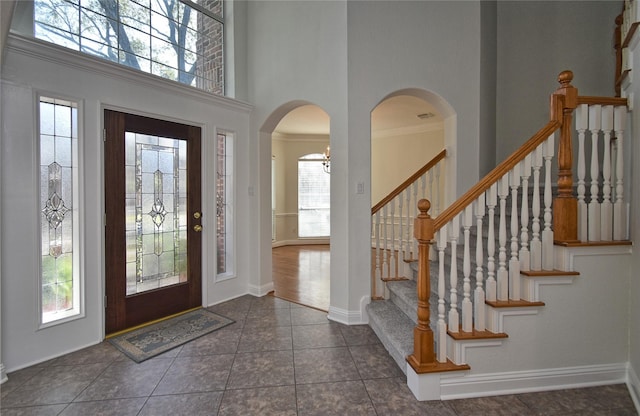 tiled foyer entrance featuring arched walkways, baseboards, stairs, and a high ceiling