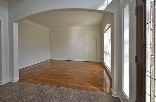 unfurnished room featuring arched walkways, baseboards, dark tile patterned floors, and ornamental molding