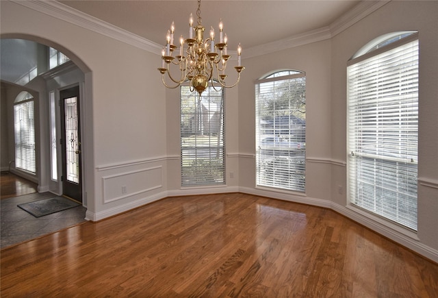 unfurnished dining area with arched walkways, a chandelier, ornamental molding, and wood finished floors