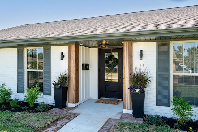 doorway to property featuring brick siding, a porch, and a shingled roof