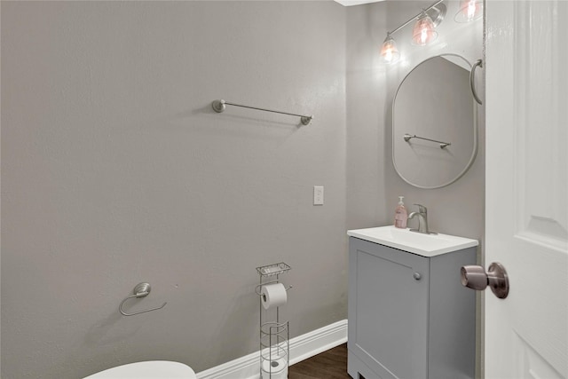 half bath with toilet, vanity, baseboards, and wood finished floors