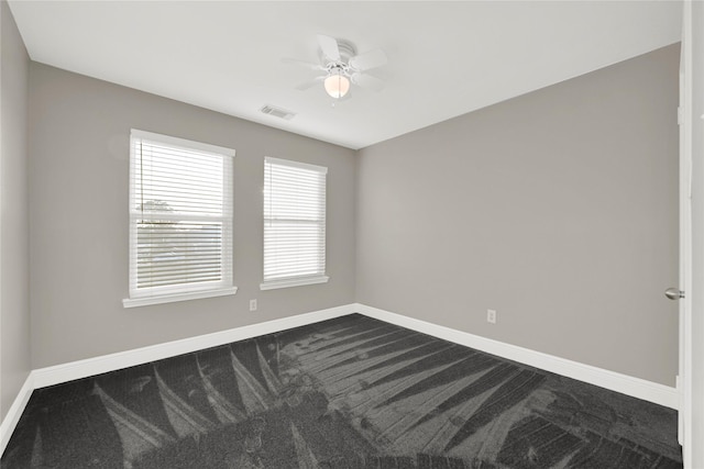 spare room featuring visible vents, baseboards, a ceiling fan, and dark colored carpet