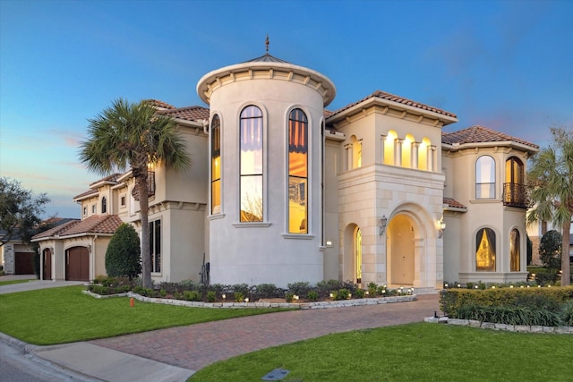 mediterranean / spanish-style home featuring stucco siding, driveway, a front yard, and a tiled roof