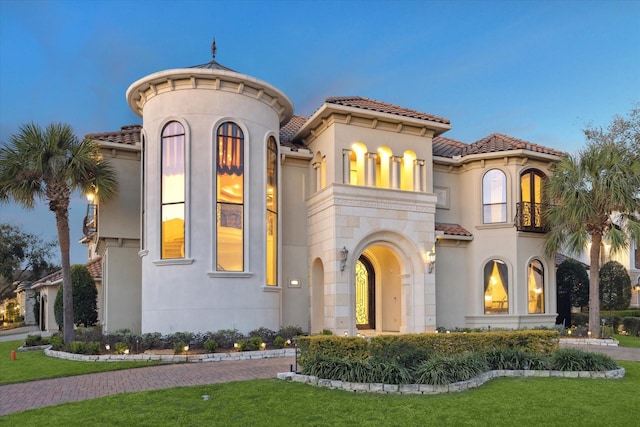 mediterranean / spanish home featuring a balcony, a tiled roof, and stucco siding