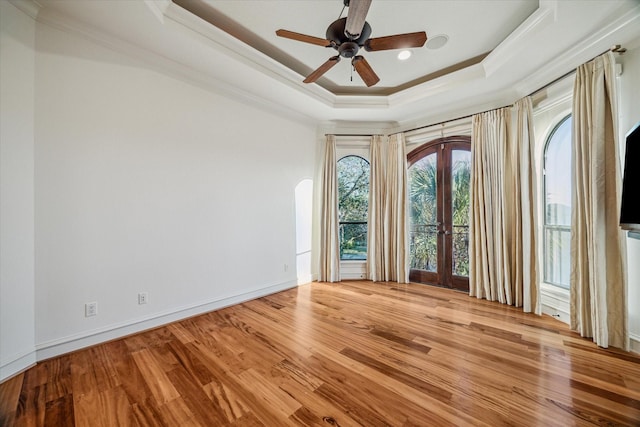 empty room with ornamental molding, a tray ceiling, wood finished floors, french doors, and ceiling fan