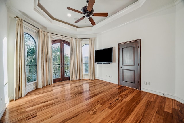 unfurnished living room featuring wood finished floors, baseboards, a tray ceiling, ornamental molding, and ceiling fan