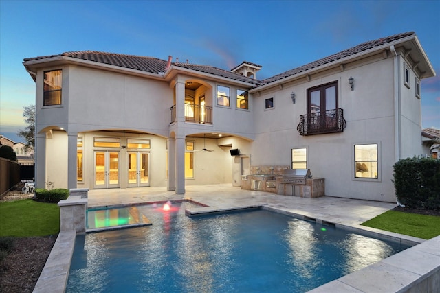 back of house at dusk featuring a tiled roof, area for grilling, french doors, and a balcony