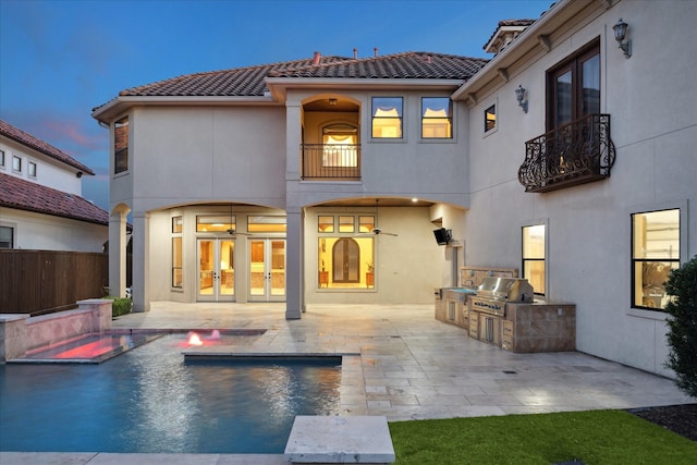 back of house at dusk with stucco siding, a patio, french doors, an outdoor kitchen, and a tiled roof