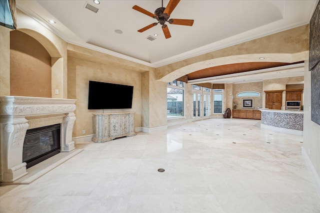 unfurnished living room featuring visible vents, a tray ceiling, a glass covered fireplace, baseboards, and ceiling fan