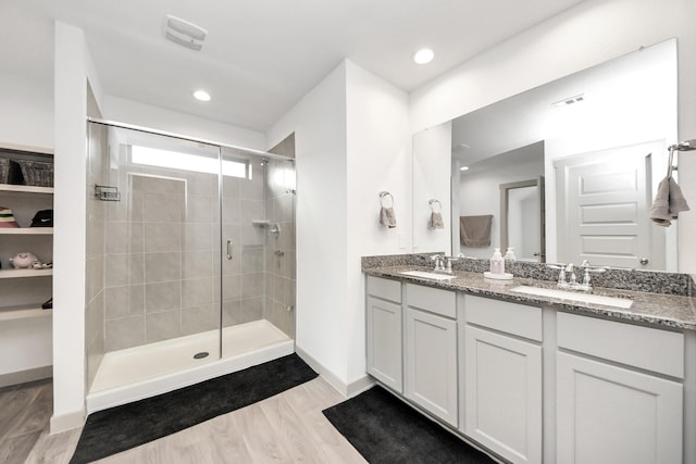 full bath featuring a shower stall, wood finished floors, double vanity, and a sink