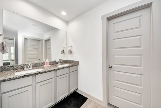 ensuite bathroom featuring a sink, ensuite bathroom, wood finished floors, and double vanity