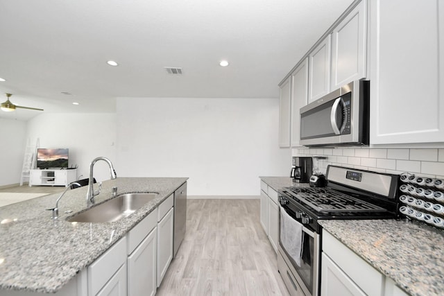 kitchen featuring a ceiling fan, a sink, tasteful backsplash, light wood-style floors, and appliances with stainless steel finishes