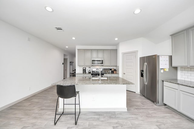 kitchen featuring visible vents, an island with sink, decorative backsplash, gray cabinets, and appliances with stainless steel finishes