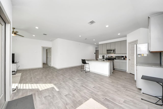 kitchen with visible vents, gray cabinetry, light wood-style flooring, stainless steel microwave, and open floor plan